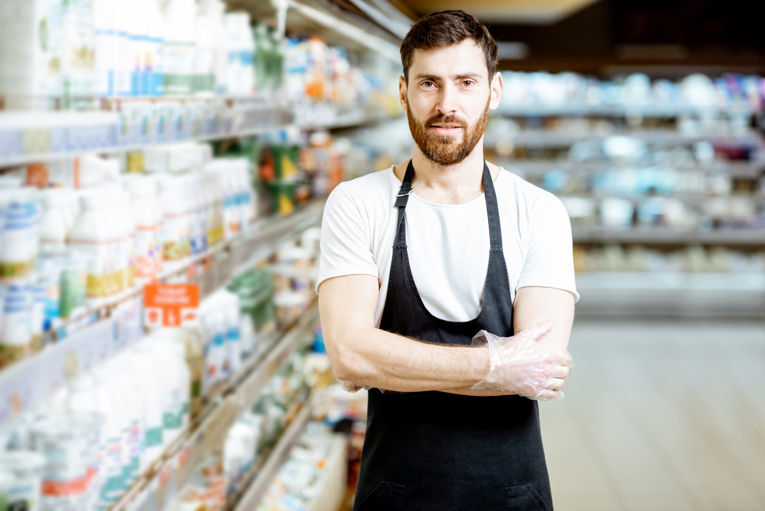 Portrait of a handsome shop worker or milkman standing near the selves with dairy products in the supermarket